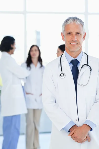 Doctor smiling while his team is communicating in the background — Stock Photo, Image