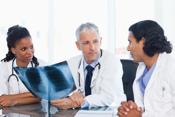 Mature doctor looking at an x-ray with two members of his team — Stock Photo, Image
