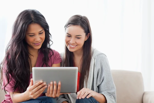 A woman holding a tablet with her friend on the couch as they wa — Stock Photo, Image