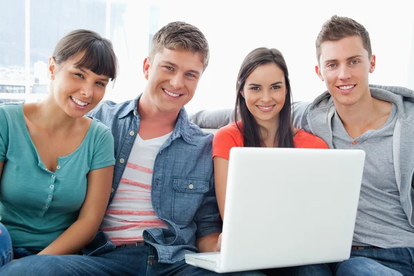 Un groupe souriant d'amis assis avec un ordinateur portable comme le — Photo