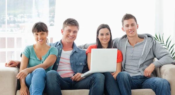 Un gruppo di amici si siede sul divano con un computer portatile mentre sembrano un — Foto Stock