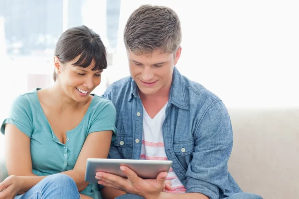 Un couple souriant s'assoit sur le canapé et utilise une tablette — Photo