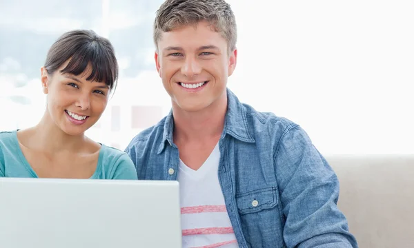 Ein Paar mit einem Laptop sitzt, während sie lächeln und in das c schauen — Stockfoto