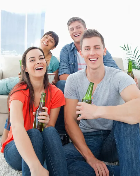 Eine lachende Gruppe sitzt auf der Couch und dem Boden mit Bier i — Stockfoto