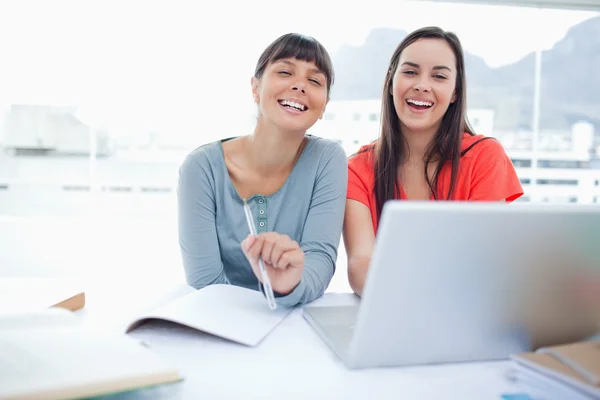 Две смеющиеся девушки сидят вместе перед ноутбуком, когда они — стоковое фото