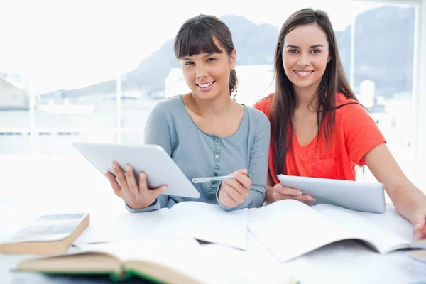 A pair of smiling girls doing work with tablets as they look int — Stock Photo, Image