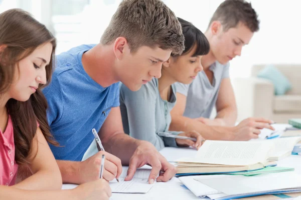 Seitenansicht von vier Studenten, die gemeinsam lernen und schreiben — Stockfoto