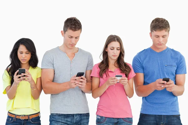 Four standing beside each other and texting on their phon — Stock Photo, Image