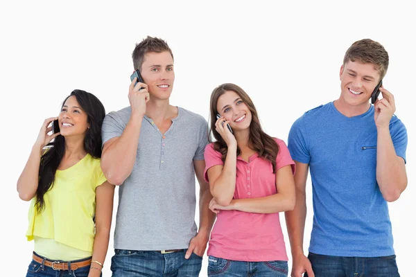Four all on their phones as they stand beside each other — Stock Photo, Image