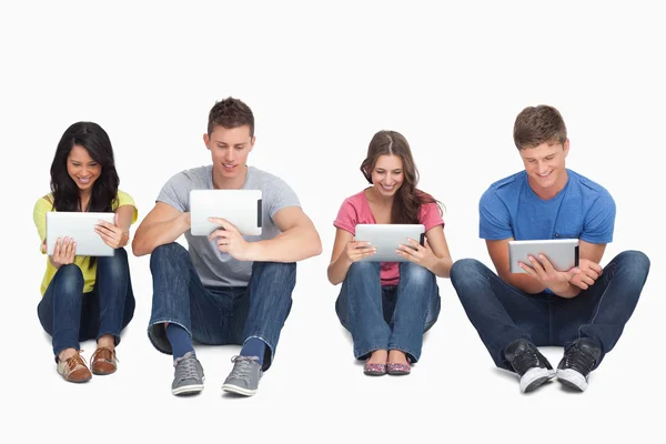 Four friends sitting on the ground all with tablets — Stock Photo, Image