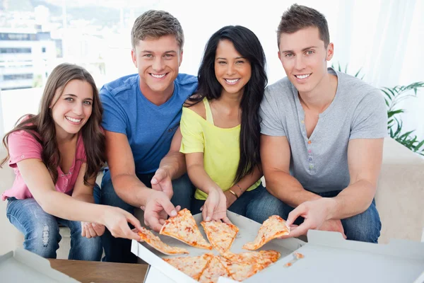 Eine Gruppe von Freunden, die jeweils ein Stück Pizza zu sich nehmen, während sie sich — Stockfoto