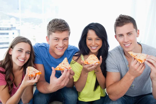 Freunde, die gerade ihre Pizza essen, während sie in die Kamera schauen — Stockfoto