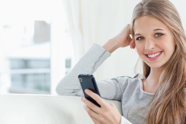 En leende flicka med en telefon i handen som hon ser på kameran — Stockfoto