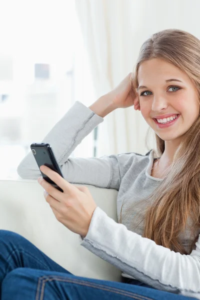 Une fille souriante tient un téléphone dans sa main alors qu'elle regarde la caméra — Photo