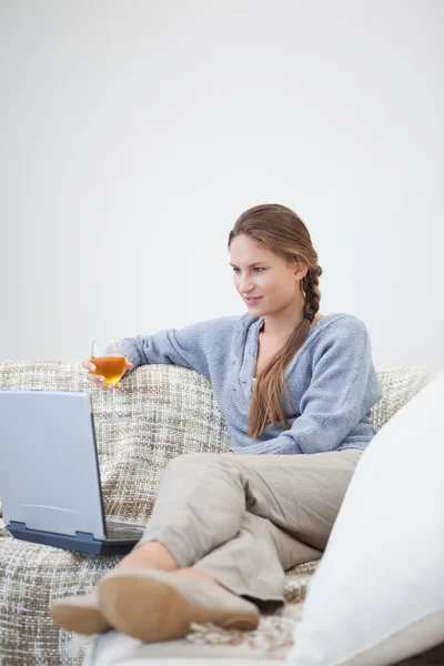 Woman sitting and holding a glass while looking on a laptop — Stock Photo, Image