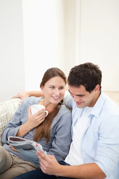 Couple sitting on a sofa while reading a newspaper — Stock Photo, Image