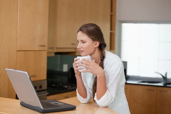 Женщина держит чашку, глядя на компьютер — стоковое фото