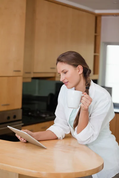 Donna che tiene in mano una tazza mentre guarda un tablet — Foto Stock