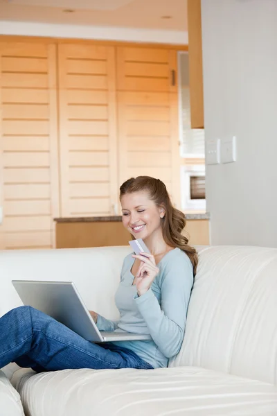 Woman using a laptop while holding a card — Stock Photo, Image