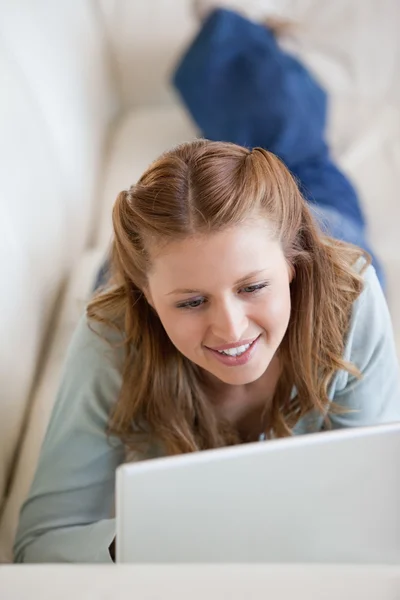 Frau liegt auf einem Sofa, während sie einen Computer benutzt — Stockfoto