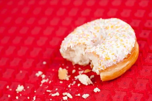 Half eaten doughnut on a red tablecloth — Stock Photo, Image