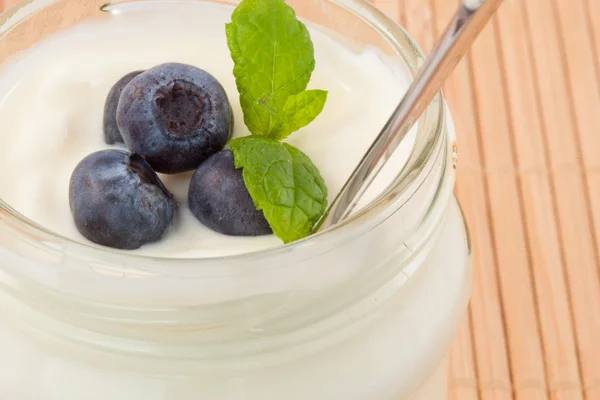 Närbild på fyra blåbär i en kastrull med yoghurt — Stockfoto
