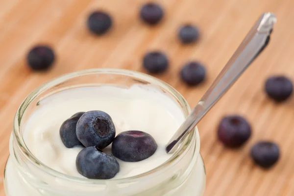 Närbild på en gryta med yoghurt med blåbär visas bakom — Stockfoto