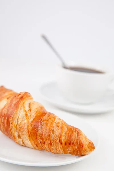 Croissant y una taza de café con una cuchara en platos blancos —  Fotos de Stock