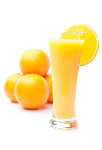 Haufen Orangen hinter einem Glas Orangensaft — Stockfoto