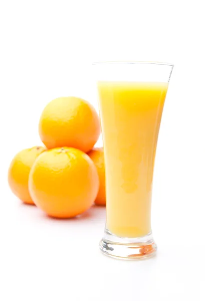 Montón de naranjas detrás de un vaso de jugo de naranja — Foto de Stock