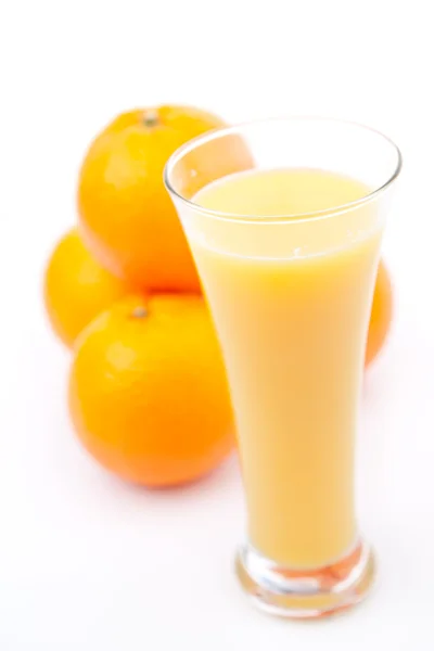 Πορτοκάλια πίσω από ένα ποτήρι χυμό πορτοκαλιού — Φωτογραφία Αρχείου