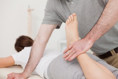 Physiotherapist bending the leg of his peaceful patient clipart