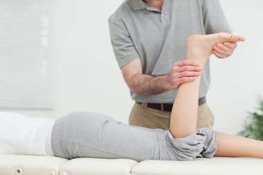 Woman lying forward while a physiotherapist examining her leg clipart