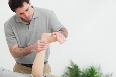 Brown-haired therapist stretching the foot of a patient clipart