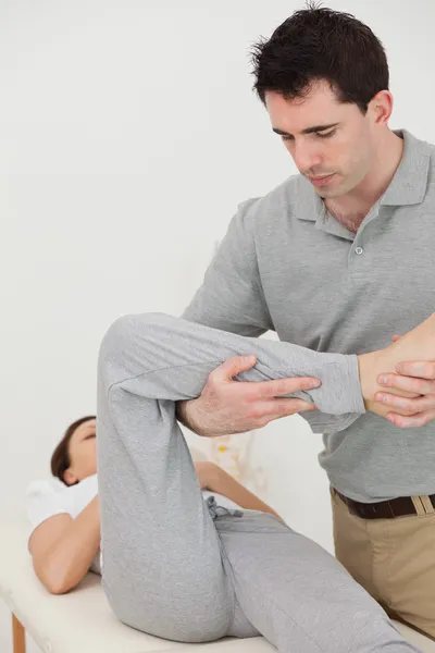 Brünette Physiotherapeutin streckt einem Patienten das Bein — Stockfoto