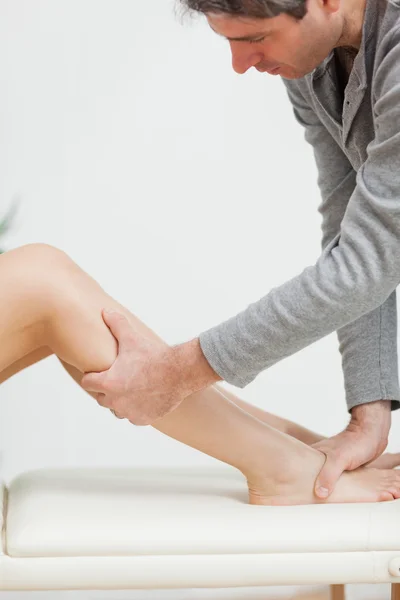 Serious osteopath holding the calf of a patient — Stock Photo, Image