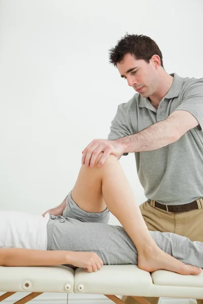 Fisioterapeuta sério esticando uma perna enquanto está de pé — Fotografia de Stock