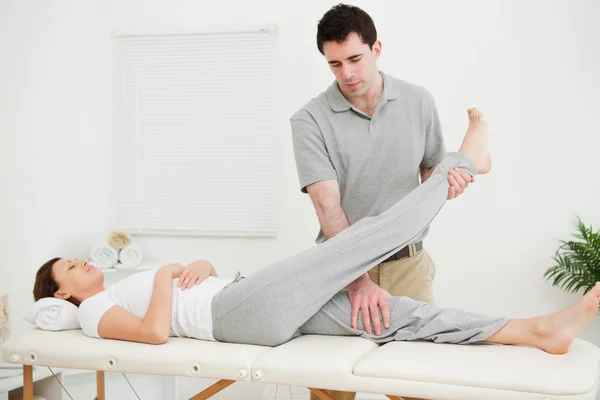 Brünette Physiotherapeutin hebt das Bein einer Patientin — Stockfoto