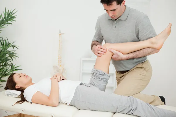 Serious osteopath bending the leg of a patient — Stock Photo, Image