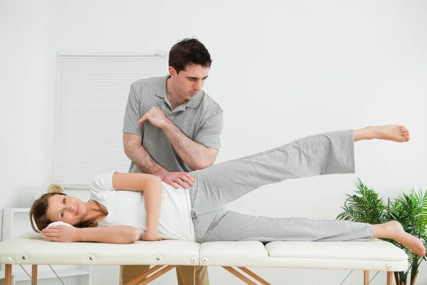 Doctor pressing his elbow on her hip while woman raising her leg — Stock Photo, Image