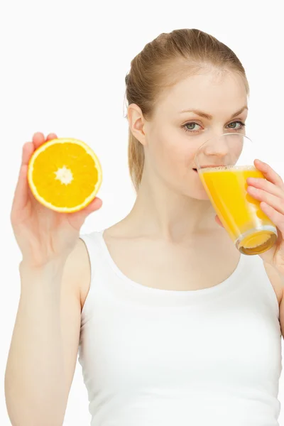 Mujer bebiendo en un vaso mientras presenta una naranja —  Fotos de Stock