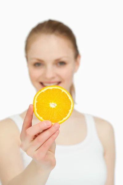 Mulher apresentando uma fatia de laranja enquanto sorri — Fotografia de Stock