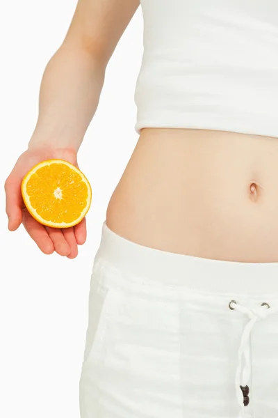 Крупным планом женщина кладет апельсин рядом с животом — стоковое фото