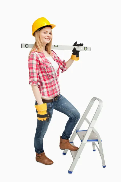 Woman holding a spirit level next to a step ladder — Stock Photo, Image