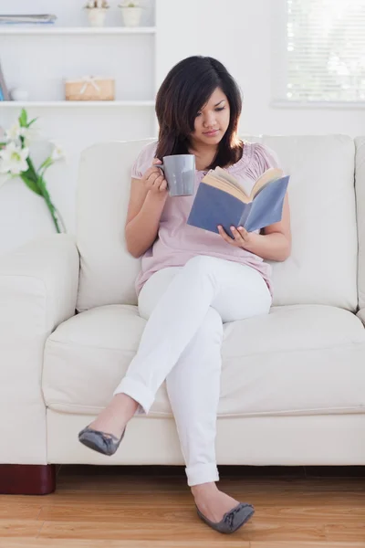 Женщина читает книгу, держа в руках кружку — стоковое фото