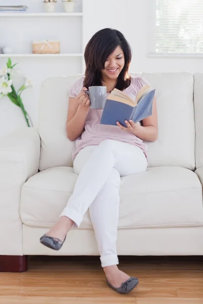 Frau liest ein Buch, während sie auf einer Couch sitzt — Stockfoto