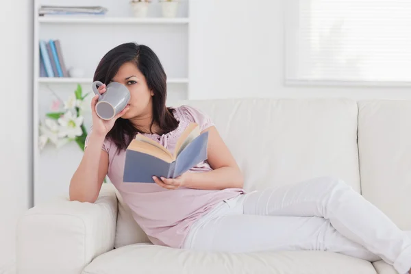 Vrouw drinken uit een beker liggend op een sofa — Stockfoto