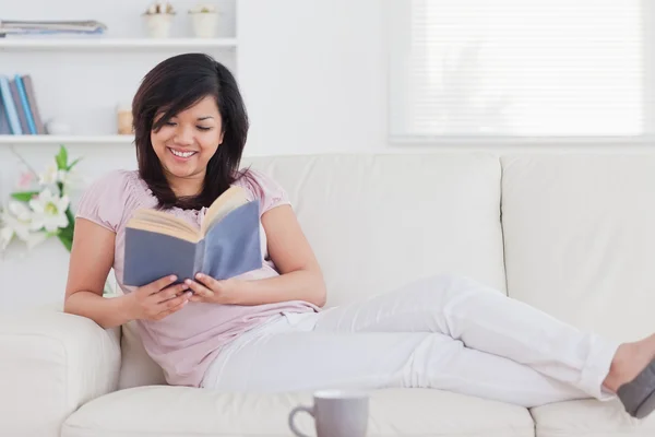 Vrouw leest een boek terwijl liggend op een sofa — Stockfoto