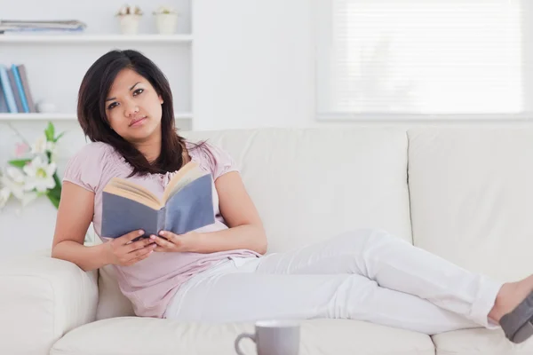 Frau liegt auf einer Couch, während sie ein Buch hält — Stockfoto