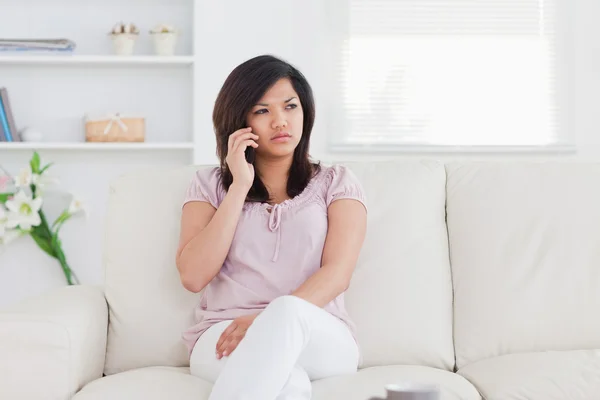 Donna seduta su un divano con un telefono in mano — Foto Stock